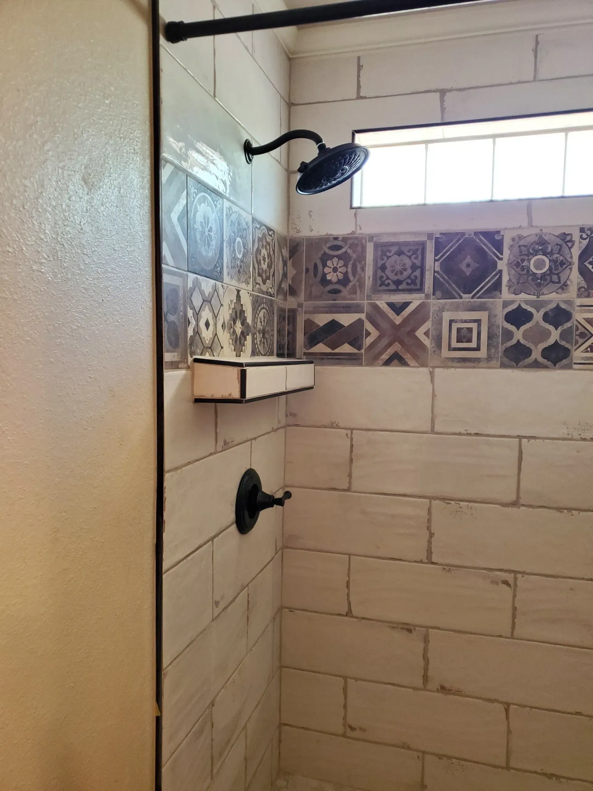 Tiled shower with two black showerheads and a frosted window above.