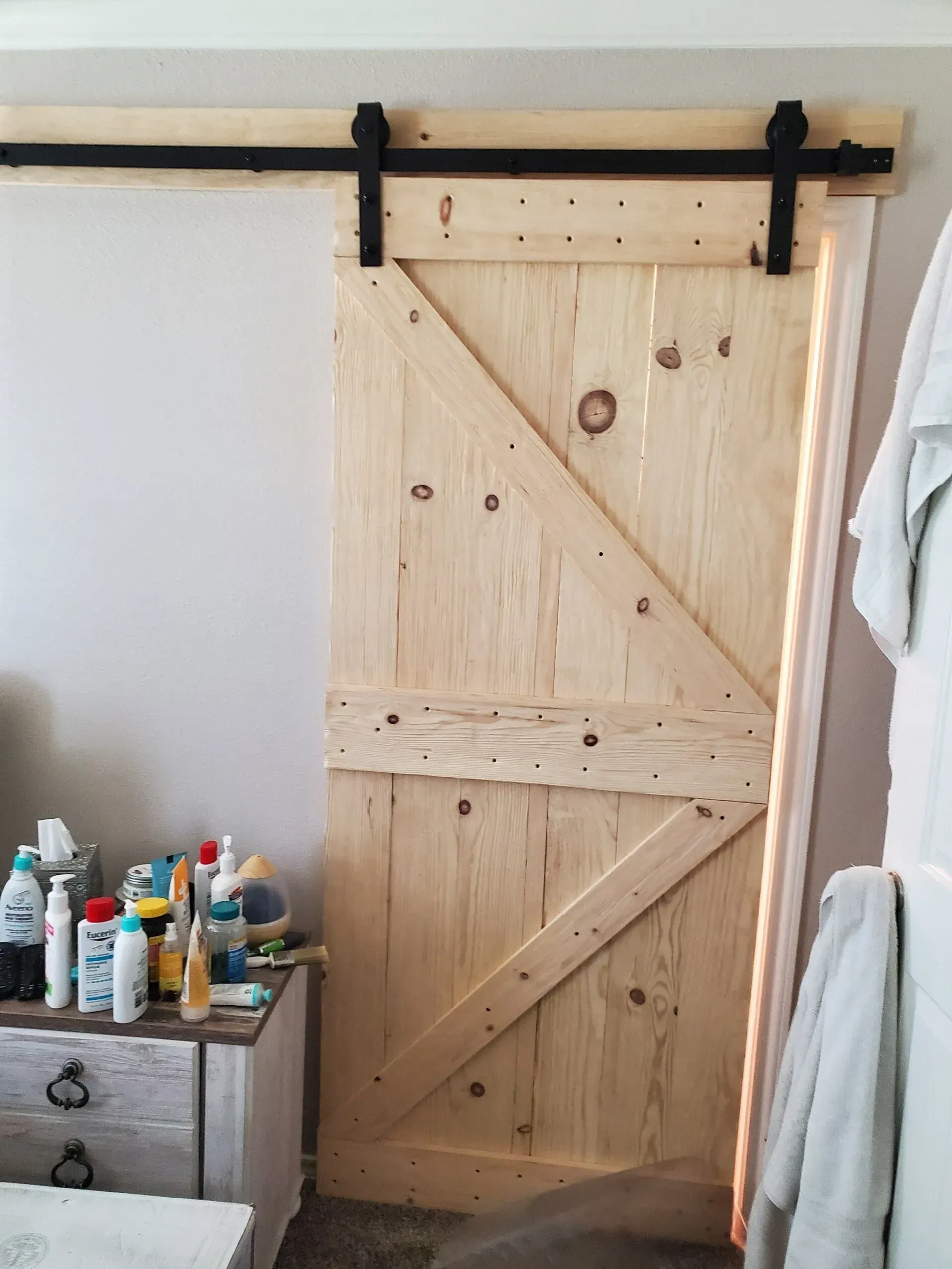 Rustic wooden sliding barn door with black track, in a room beside a dresser with bottles.