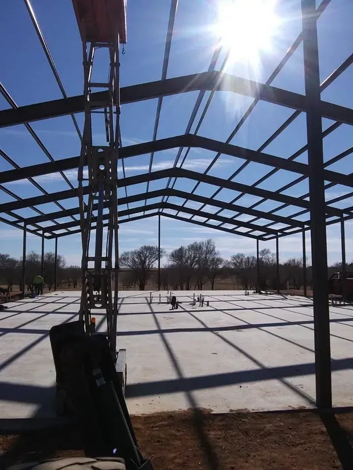 Steel frame structure under construction in bright sun, with shadows across the concrete slab.