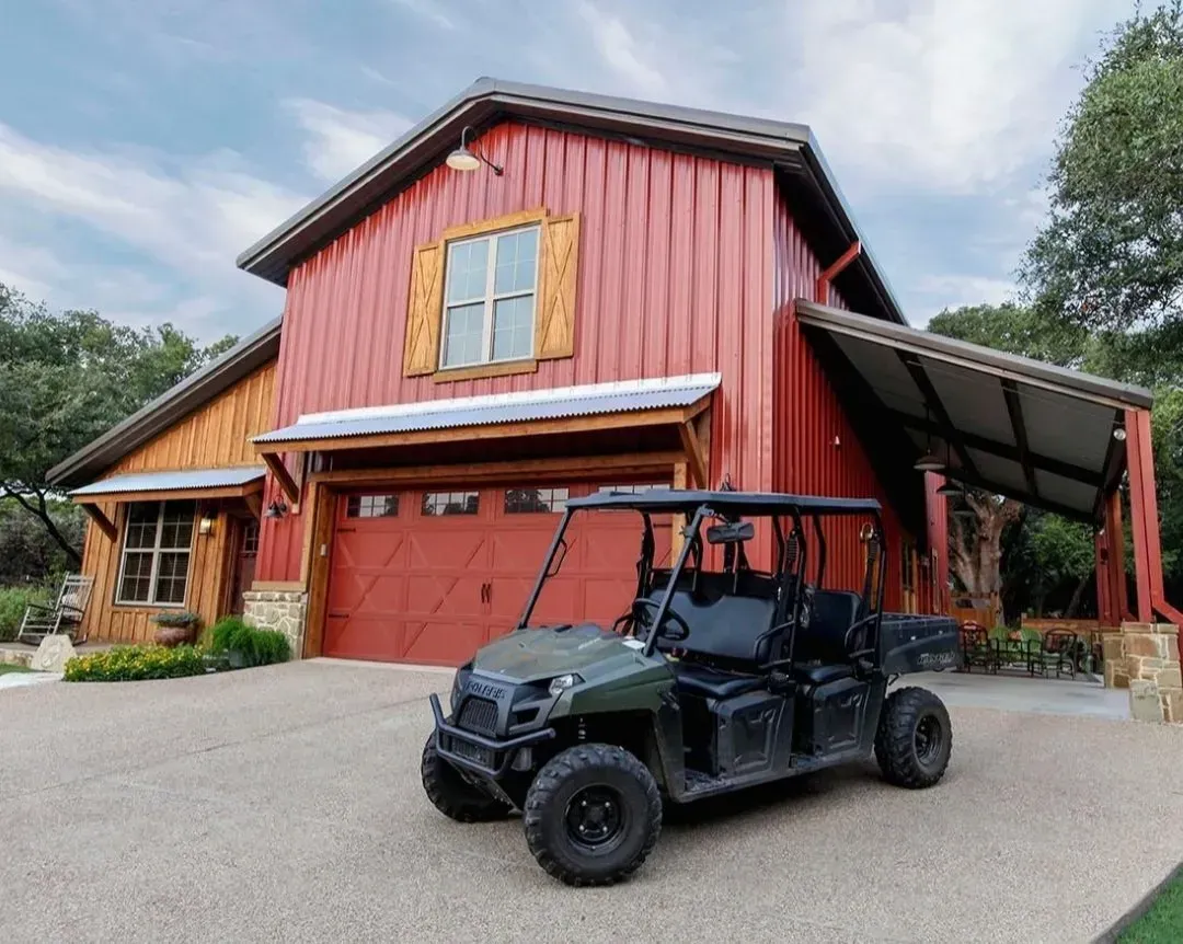 Black utility vehicle parked in front of a red barn-style house with a covered porch and gravel driveway