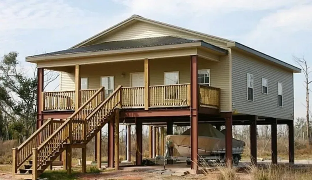 Elevated tan house on stilts with front porch and stairs in a rural setting