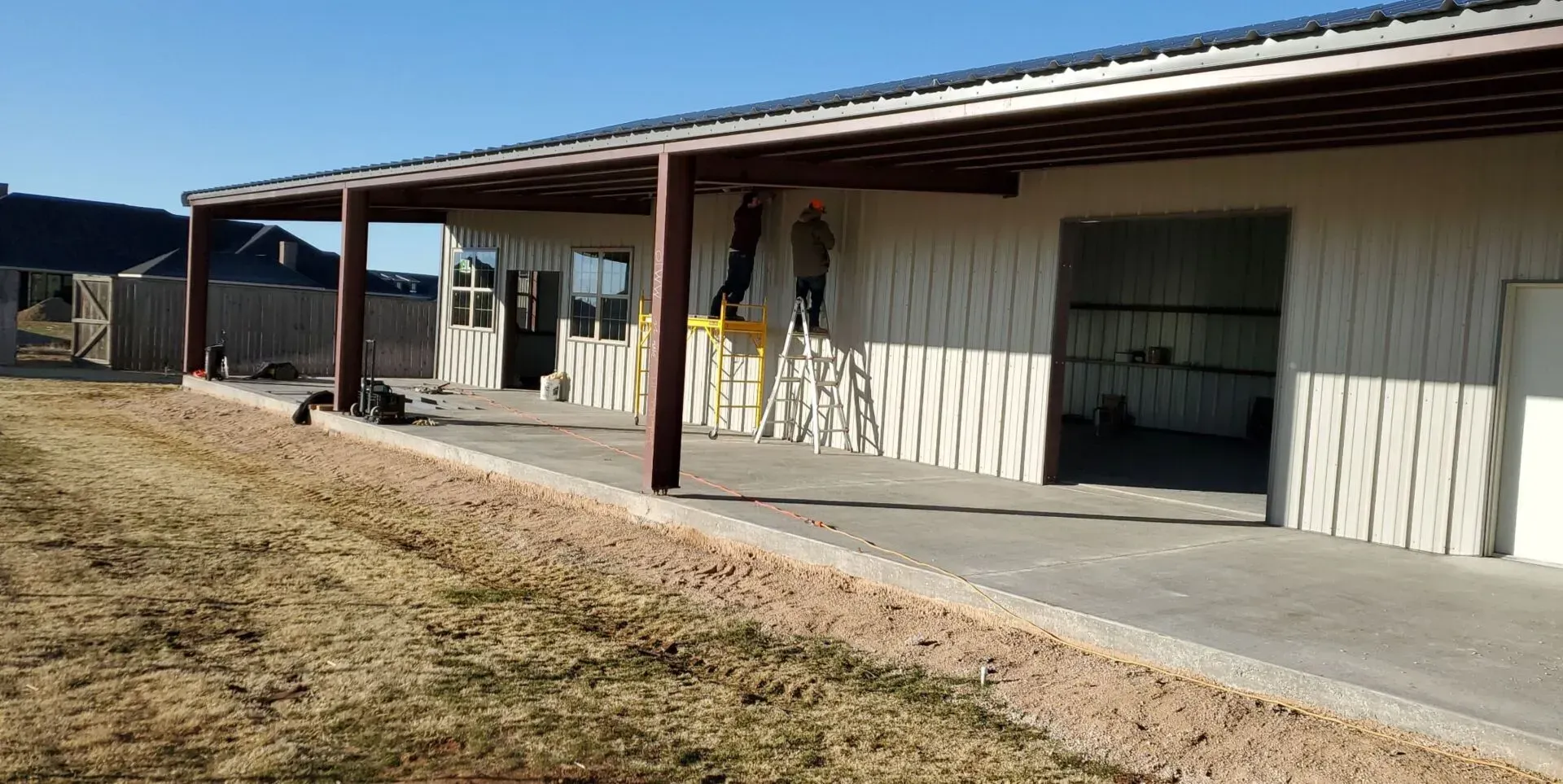 Single-story white building with a covered walkway, concrete ramp, and dry grass in front