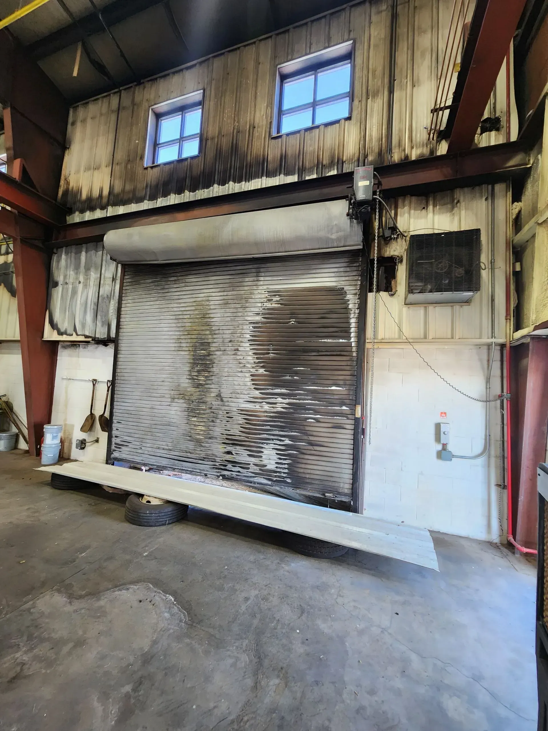 Industrial warehouse interior with a large metal roll-up door, worn walls, and concrete floor