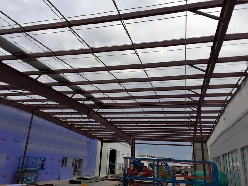 Partially built steel-roof structure with translucent panels and construction equipment inside
