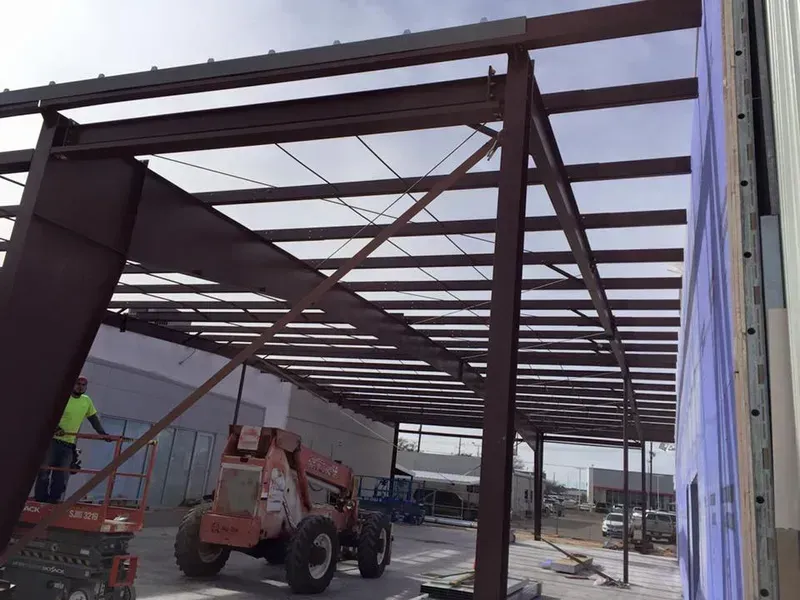 Steel frame construction inside a large warehouse with a lift and workers on site
