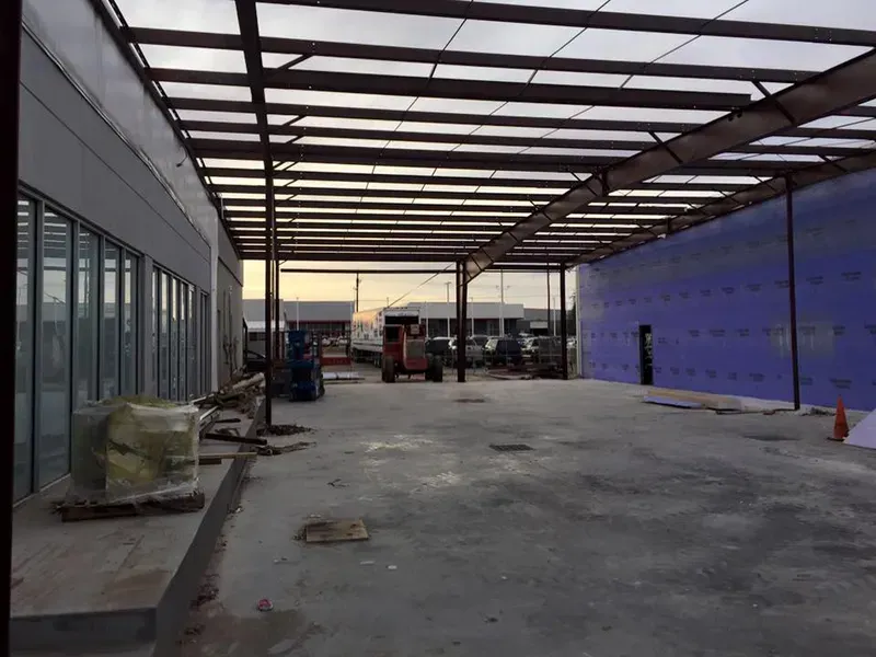 Empty construction area with concrete floor, metal roof frame, and blue wall panels at sunset