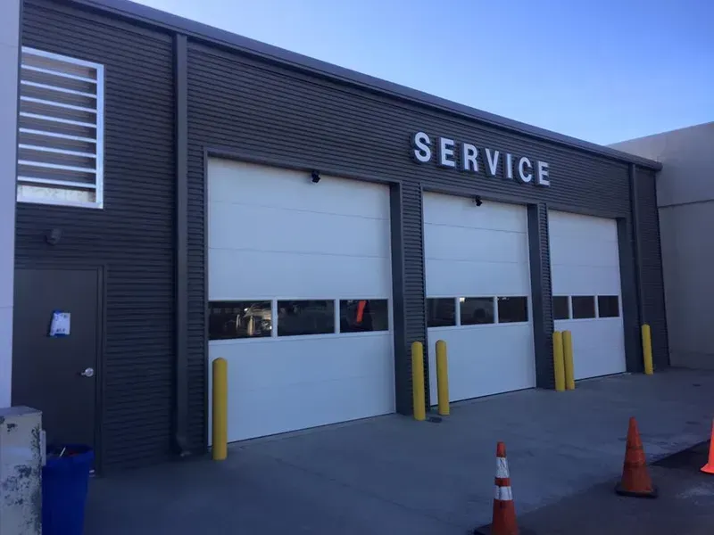 Service bay garage with white roll-up doors, yellow bollards, and orange cones outside.