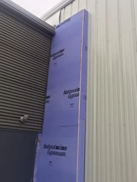 Blue insulated panel beside a gray metal wall and roller door at a building corner
