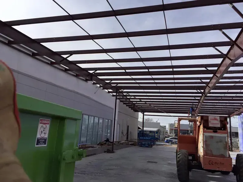 Industrial warehouse walkway with a green container, orange forklift, and metal roof framework