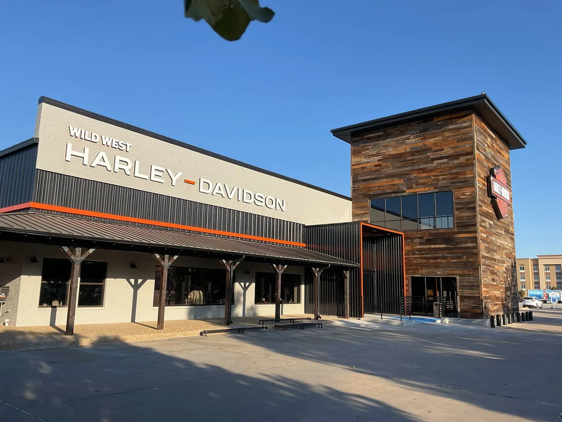 Harley-Davidson dealership exterior on a sunny day, with a stone tower and large storefront sign.