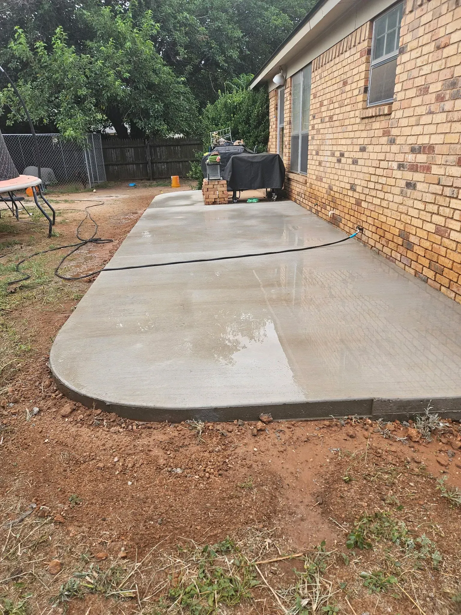 Concrete patio beside brick house with wet sections and gravel yard around it