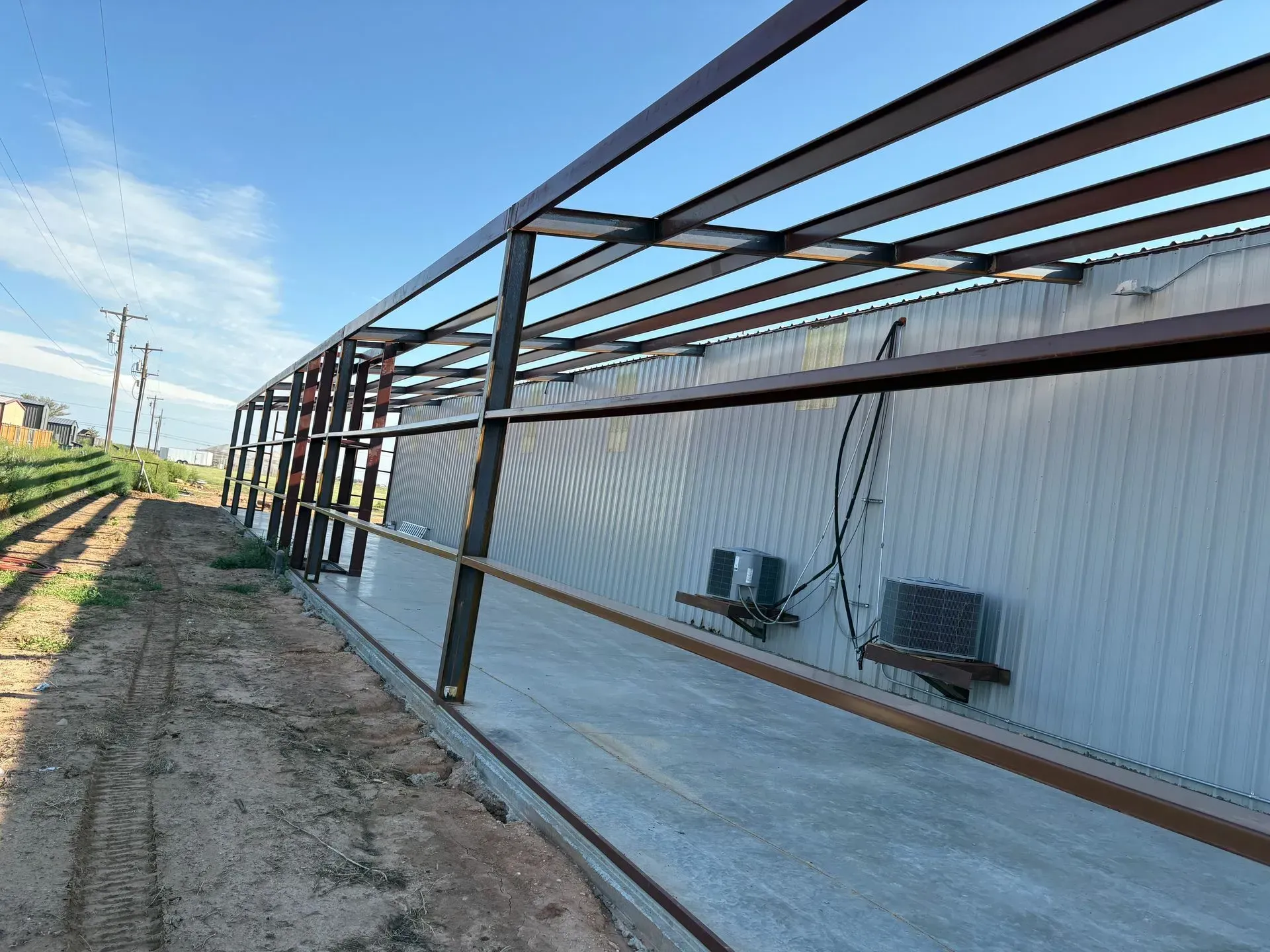 Long metal building under construction with steel framing along a gravel path in daylight