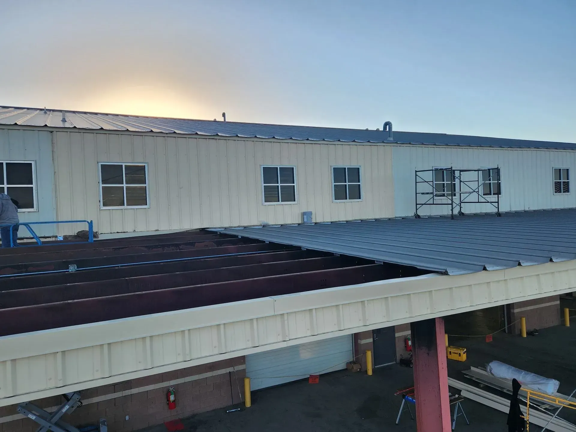 Industrial building rooftop with workers installing dark roofing panels at sunset