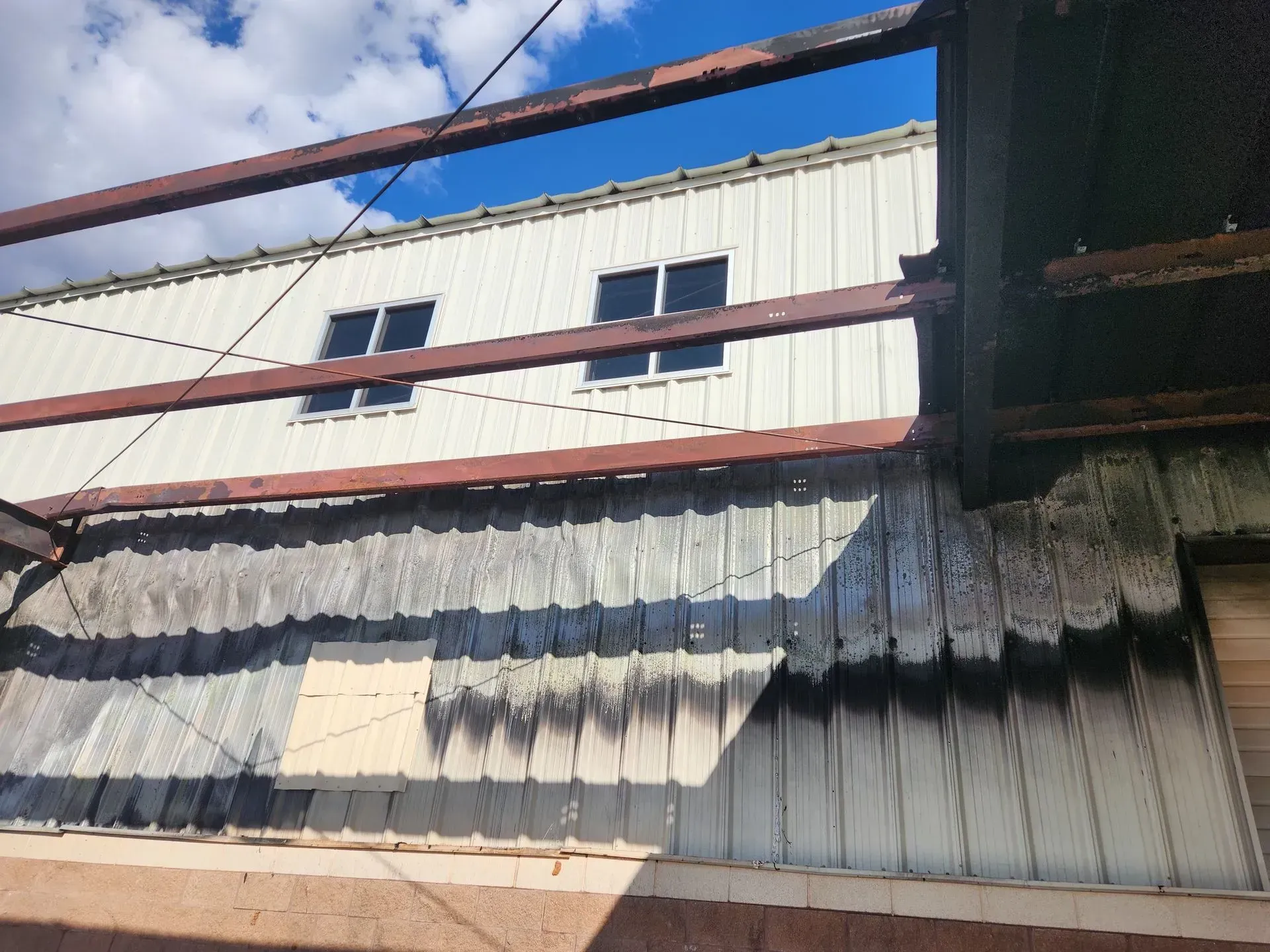 Damaged corrugated metal siding on a building with rusted beams and white upper walls