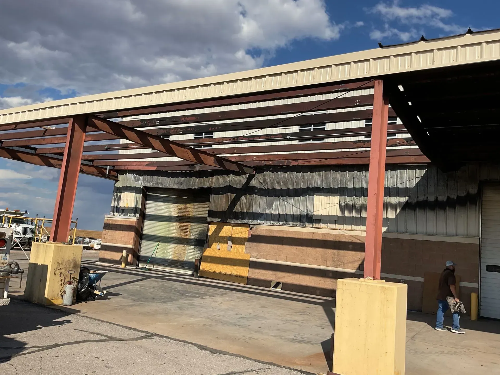 Warehouse loading dock with red steel canopy, stacked barrels, and a worker near the wall
