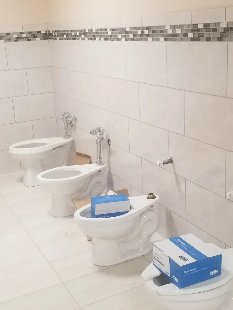 Public restroom with three white bidets and blue-and-white boxes on the fixtures
