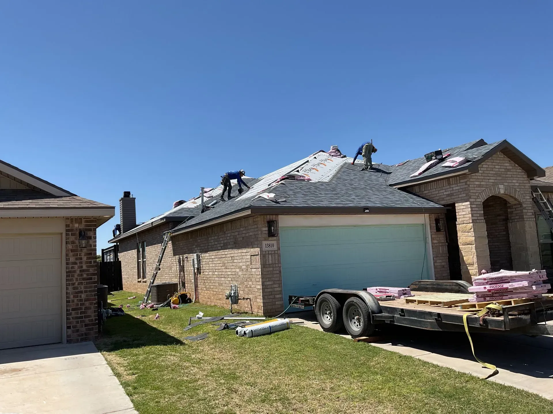 Suburban brick houses with a blue garage door and a trailer loaded with shingles in the driveway