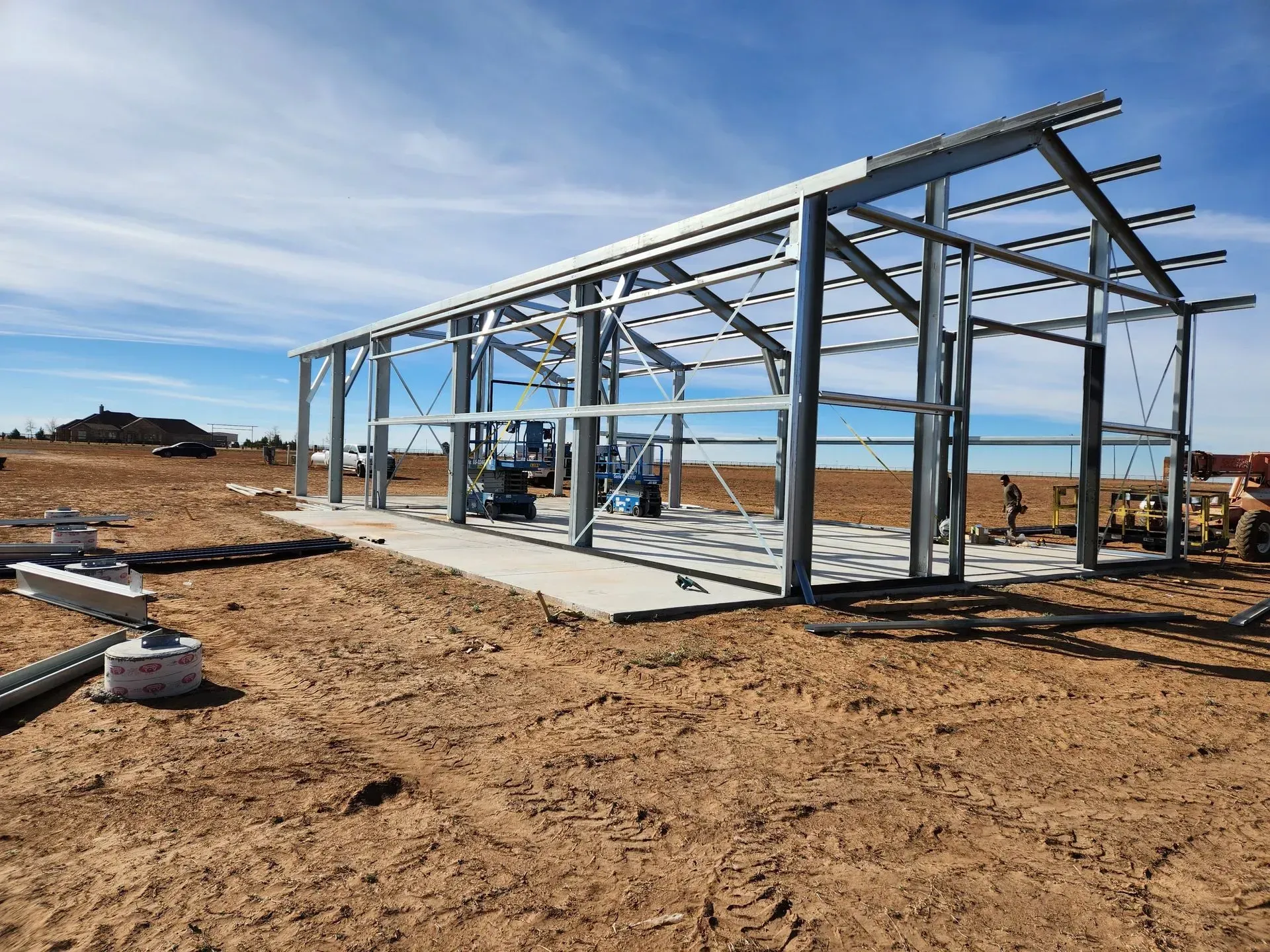 Steel frame of a building under construction on a dirt lot under a clear sky