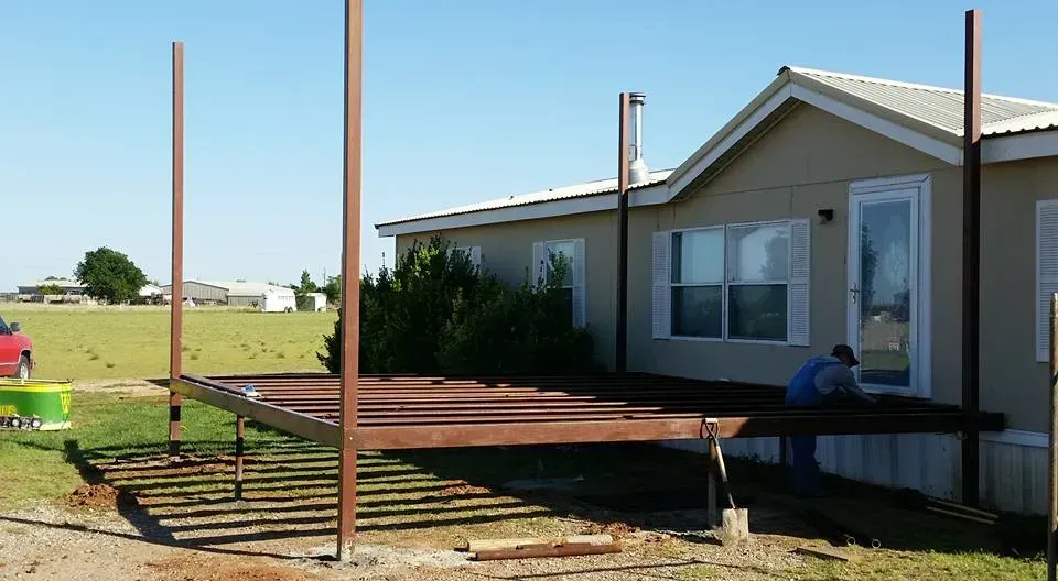 Wooden deck frame under construction beside a house, with tall support posts and railings in progress.
