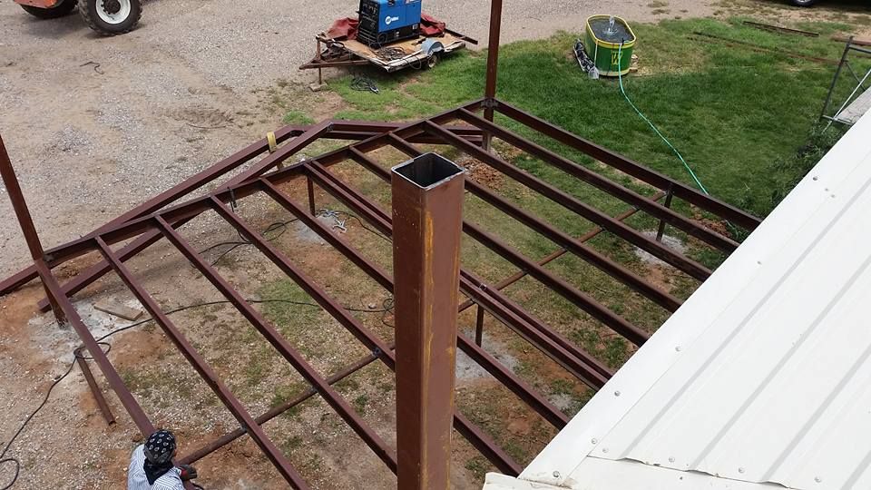 Rusty metal roof frame under construction beside a white roof edge and grassy yard