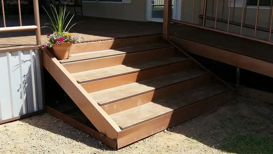 Wooden porch steps with a handrail and potted plant beside a house entrance