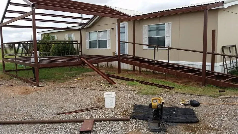 Covered patio frame beside a house, with gravel yard and construction tools in the foreground
