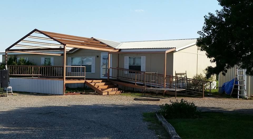 Single-story house with a ramp, porch, and gravel driveway in a sunny yard
