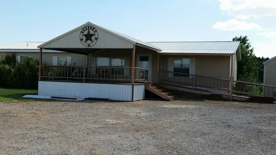 Single-story building with a covered porch, ramp, and gravel parking lot under a cloudy sky