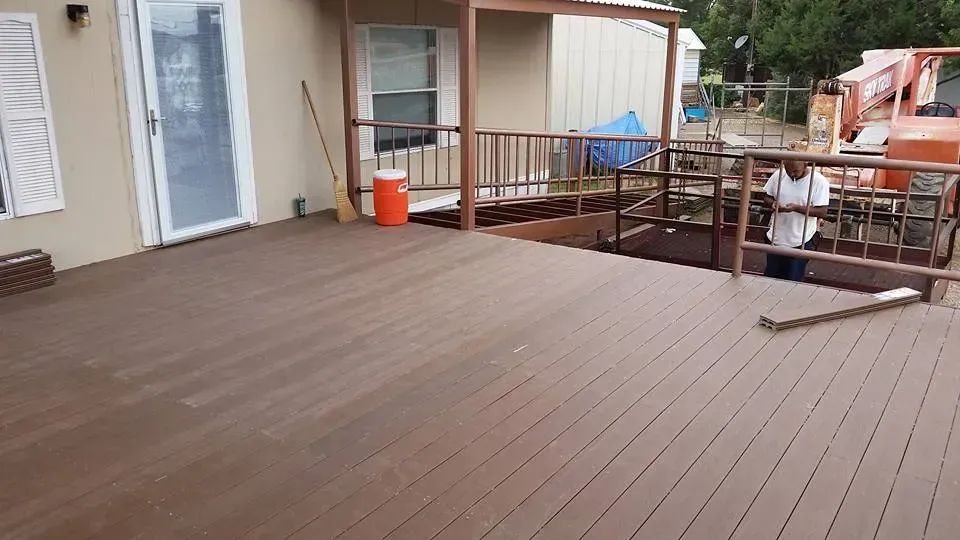 Wooden deck outside a building, with railing, chairs, and an orange bucket near the door.