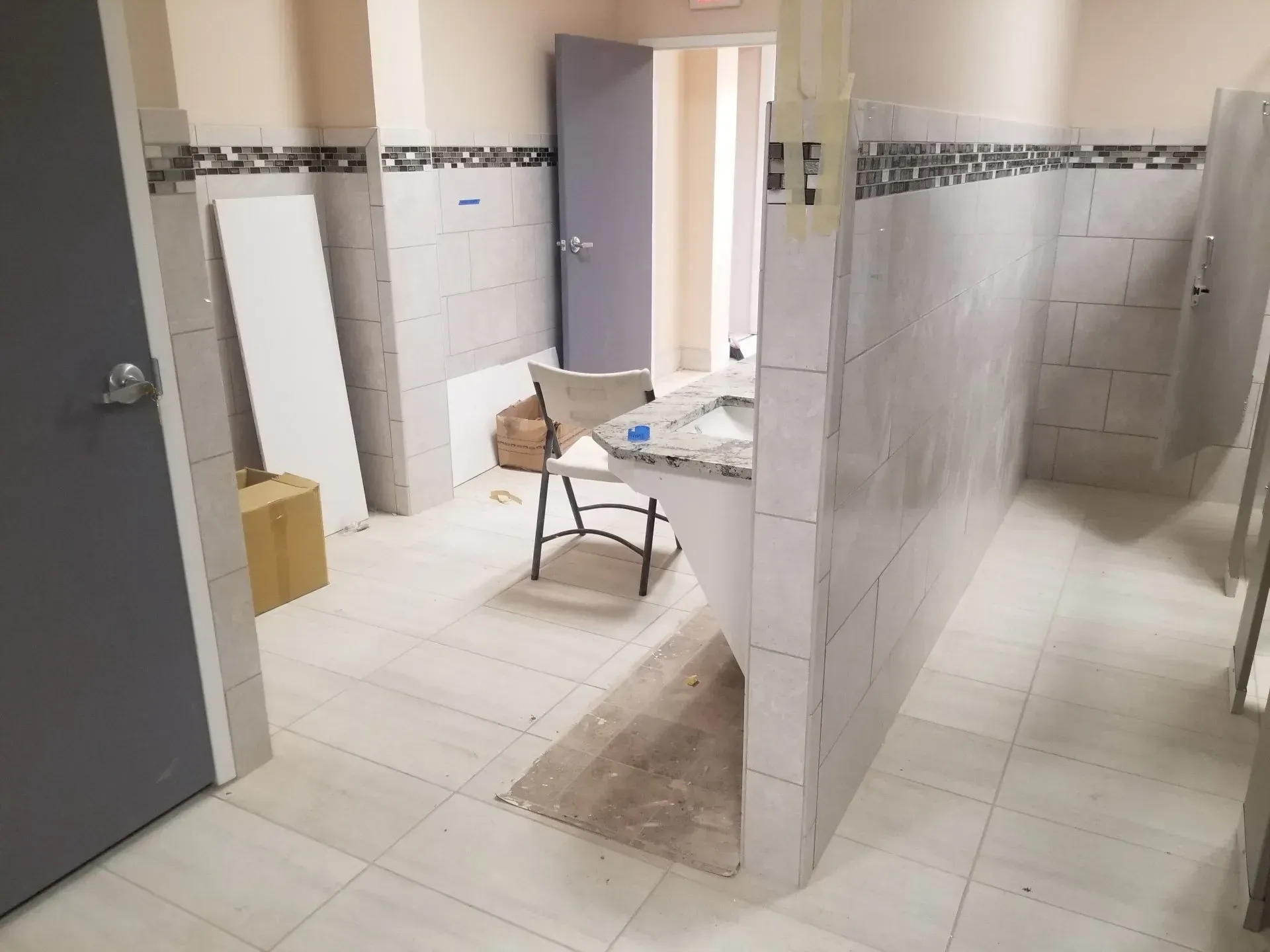 Public restroom with tiled stalls, a table and chair, and construction materials on the floor