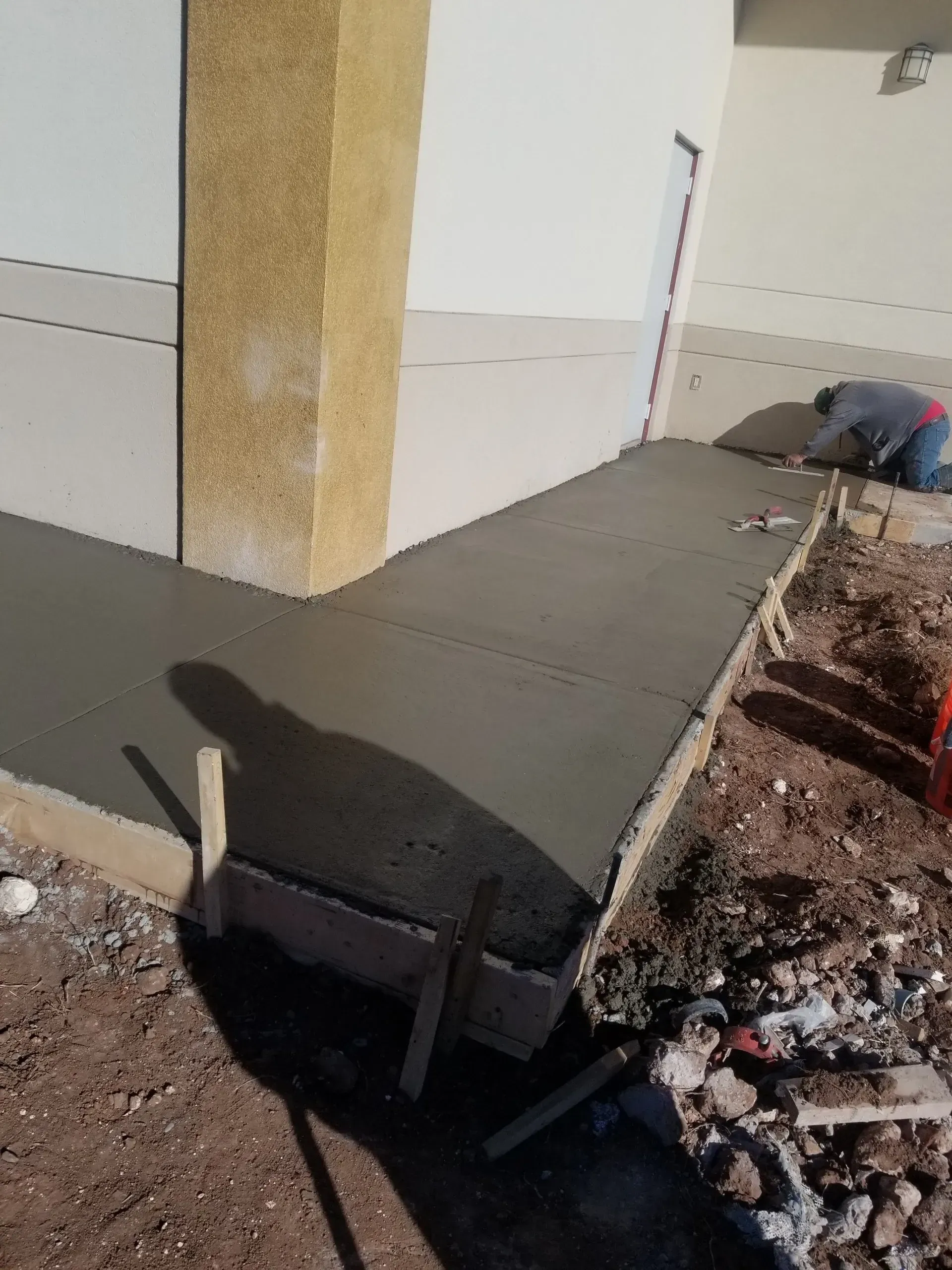 Concrete sidewalk being poured beside a building, with workers smoothing the surface.