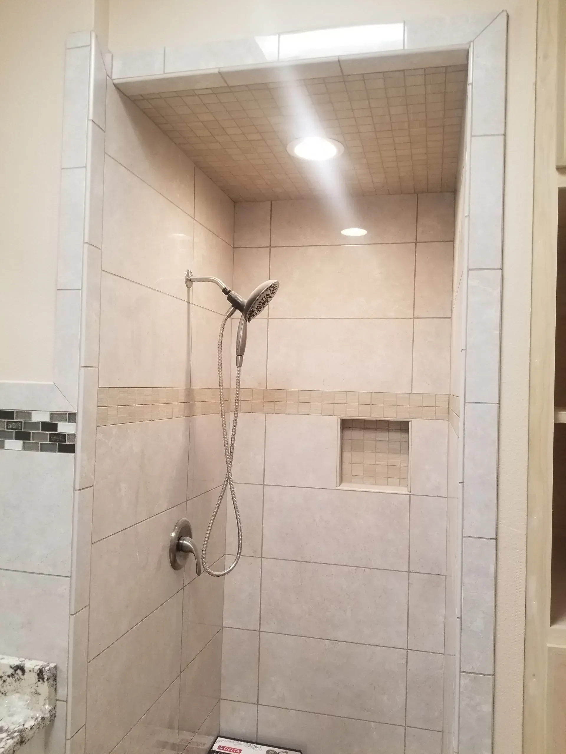 Tiled walk-in shower with handheld showerhead, built-in shelf, and beige walls
