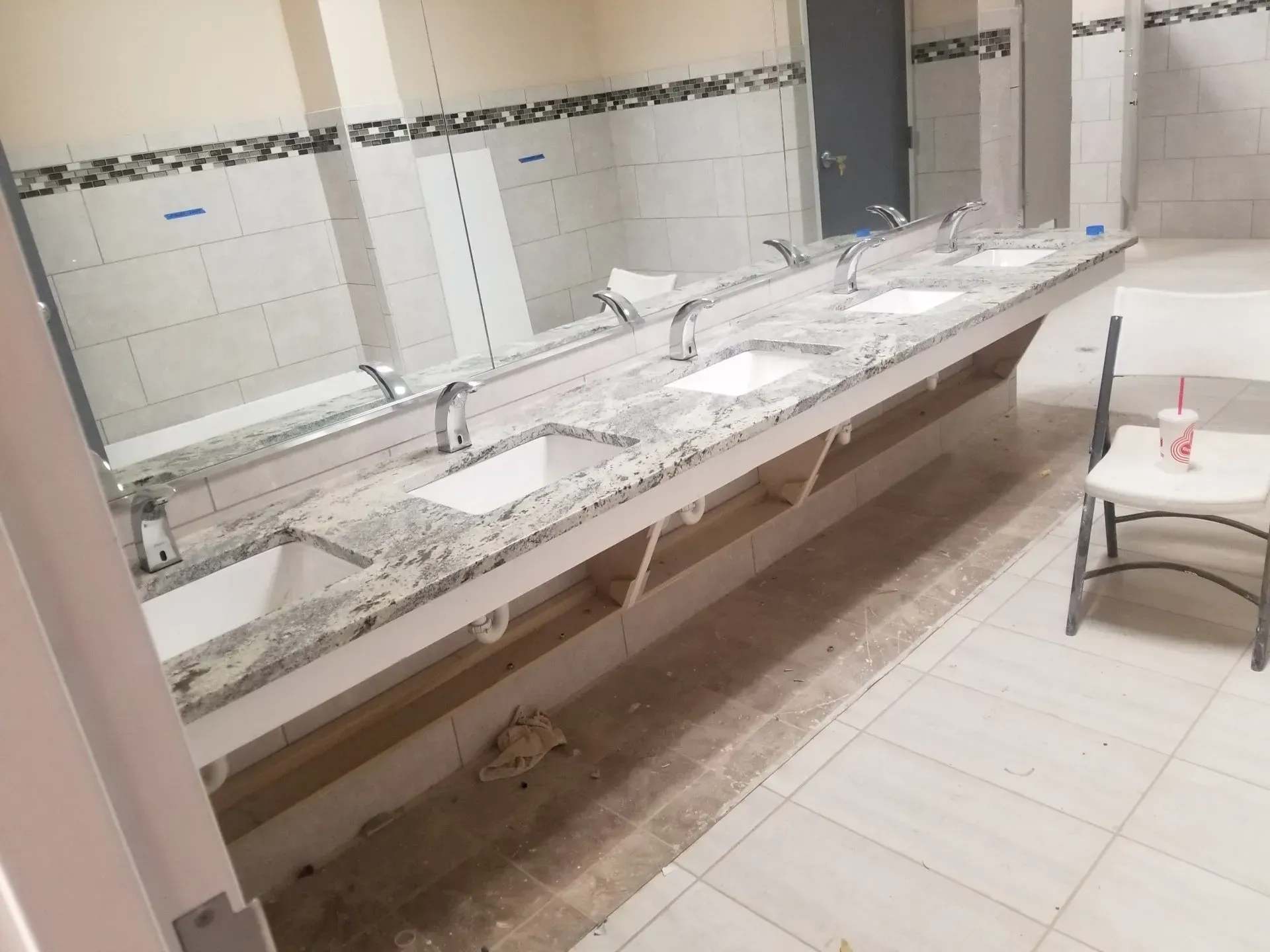 Public restroom with a long row of sinks, mirrors, and tiled walls, showing wet counters and a damp floor.