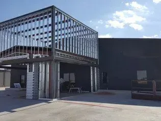 Outdoor building with a metal-framed entrance over a paved lot and a dark wall in the background