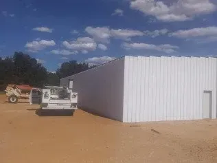 White metal building with vehicles parked on a dirt lot under a cloudy sky