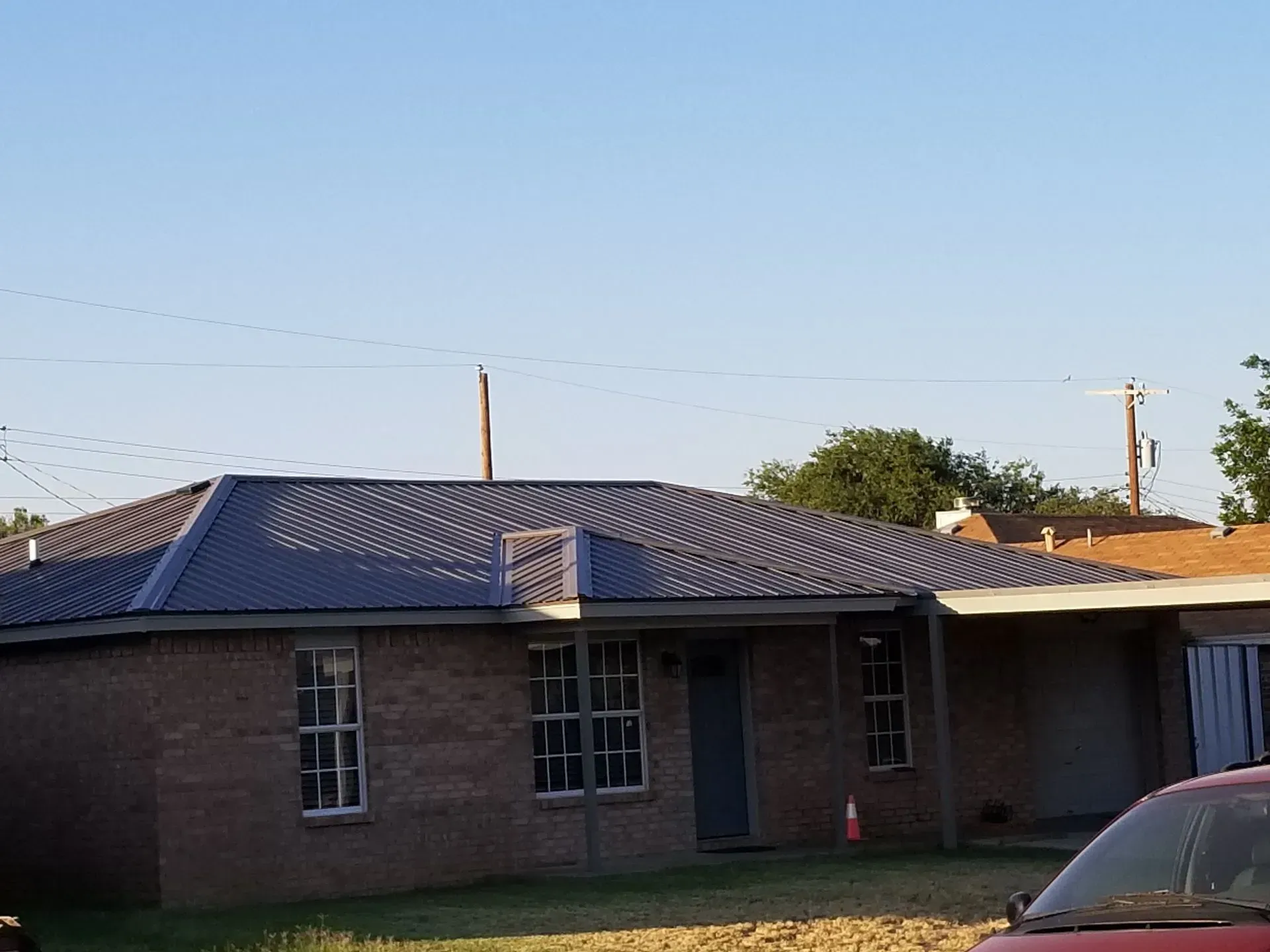 Single-story brick house with a dark roof and power lines overhead under a clear blue sky