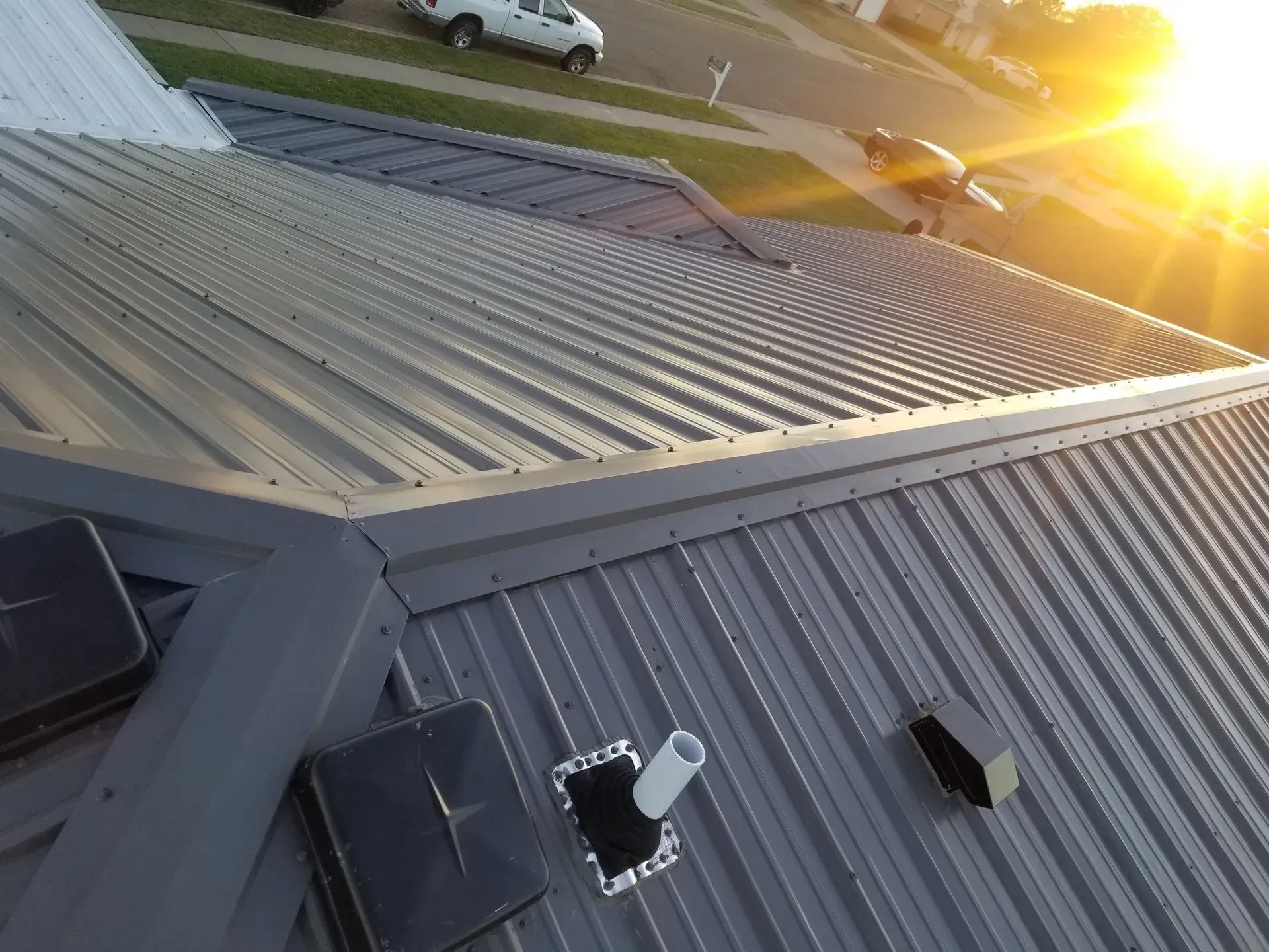 Tilted view of a corrugated metal roof at sunset with rooftop vents and bright sun glare