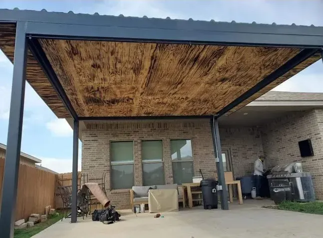 Covered backyard patio with wood ceiling, brick wall, sliding doors, and outdoor furniture on a concrete slab
