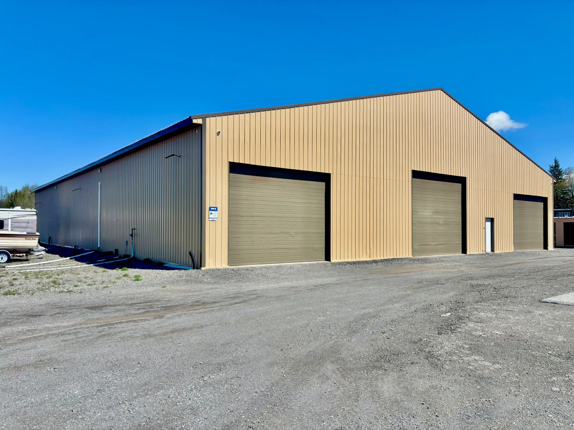 Beige metal warehouse with three garage doors on a gravel lot under a blue sky
