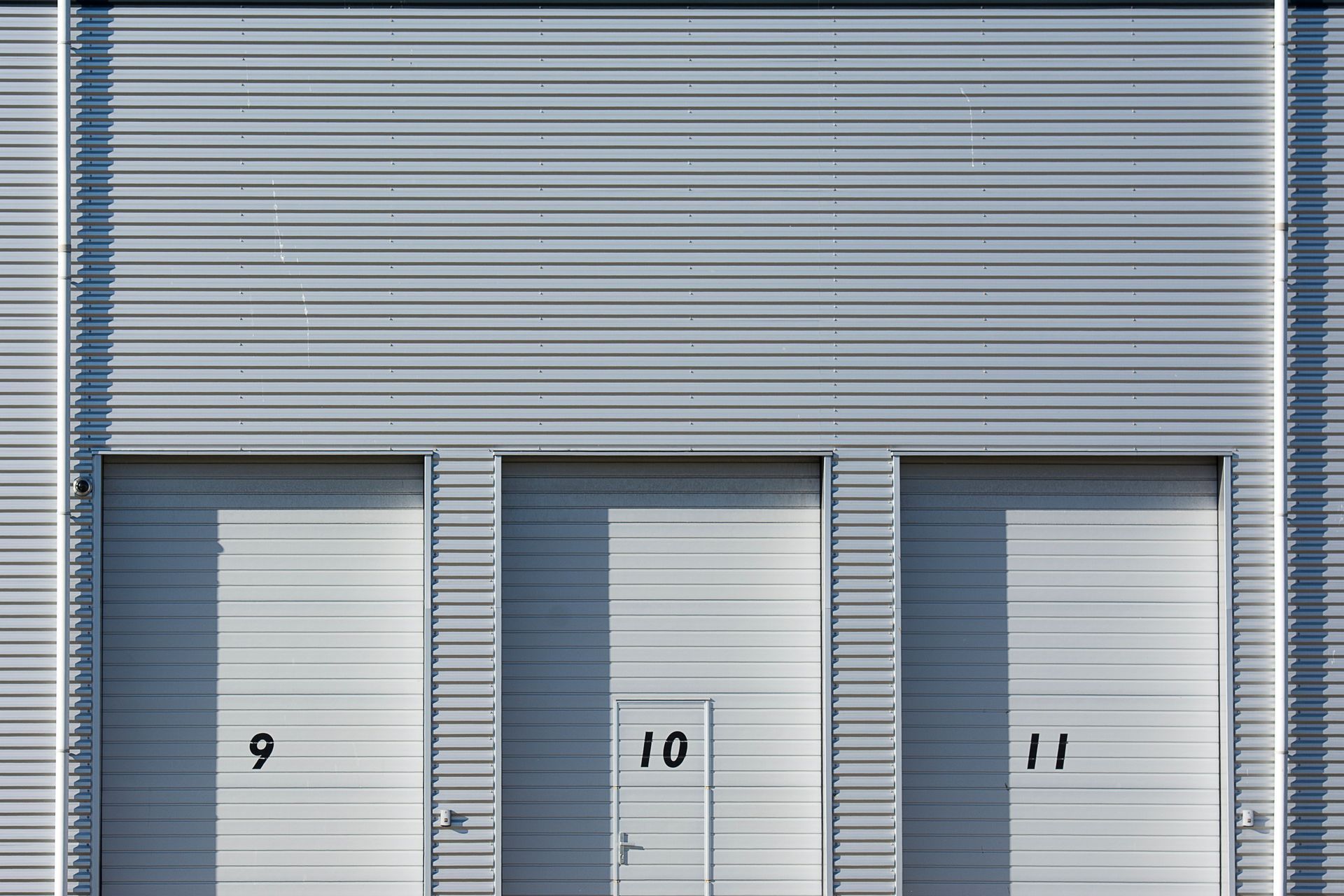 Three gray warehouse doors labeled 9, 10, and 11 on a corrugated metal building.