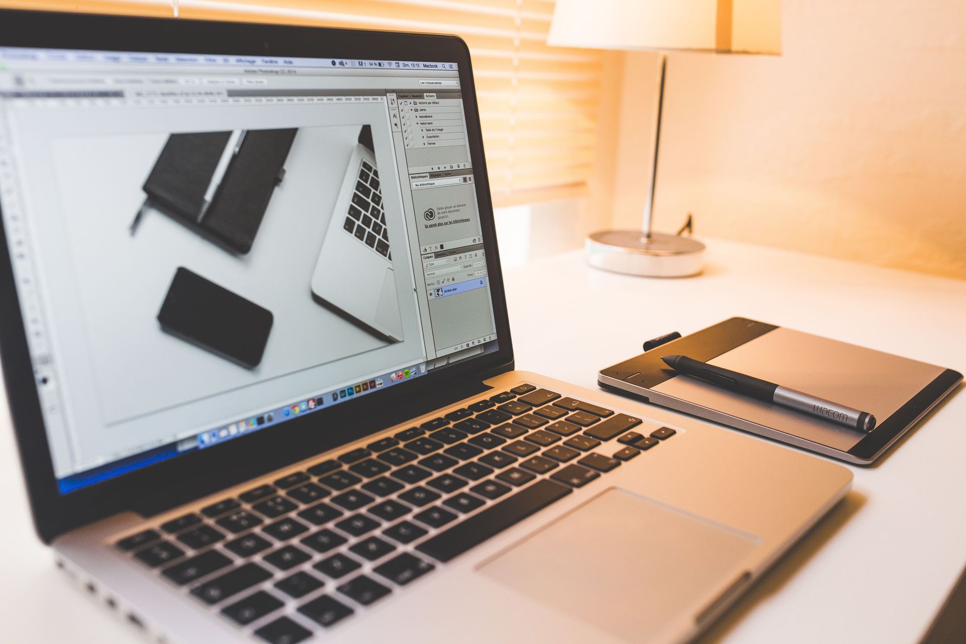 Laptop displaying design work beside a graphics tablet and a warm desk lamp.