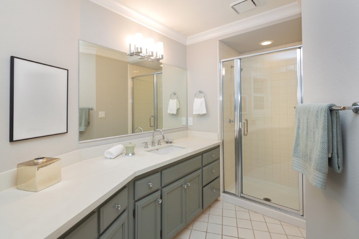 Bathroom with gray cabinets, white countertop, large mirror, and glass shower.