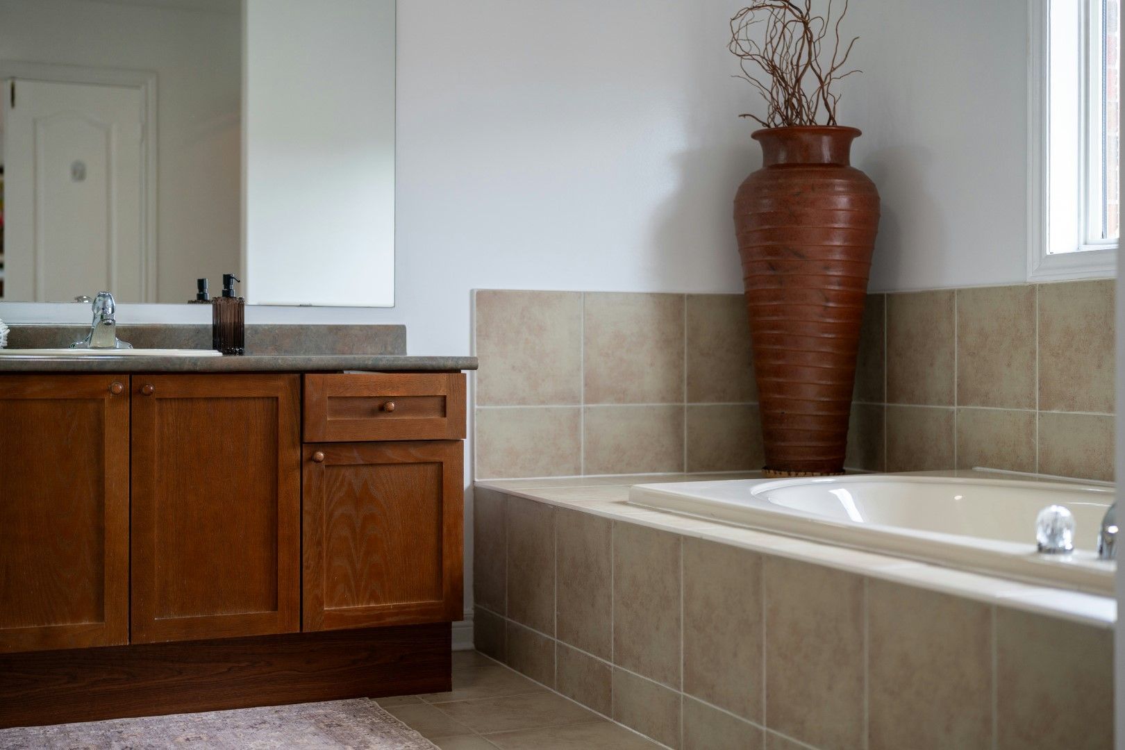 Tub surround with neutral tile, wood vanity, and decorative vase after kitchen and bathroom remodeling in Avondale, AZ