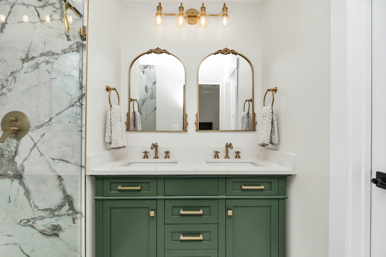 Green bathroom vanity with double mirrors, gold fixtures, and marble tile during bathroom remodeling in Avondale, AZ