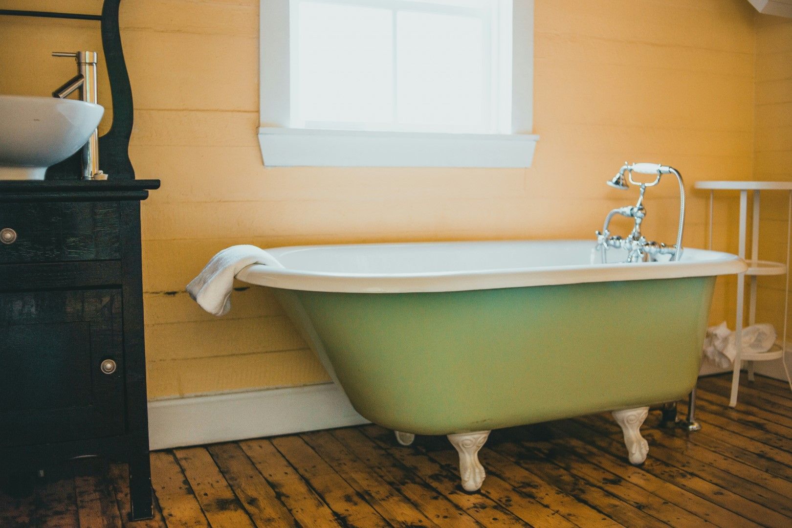 Green freestanding bathtub with vintage-style fixtures and warm tile walls after bathroom remodeling in Avondale, AZ