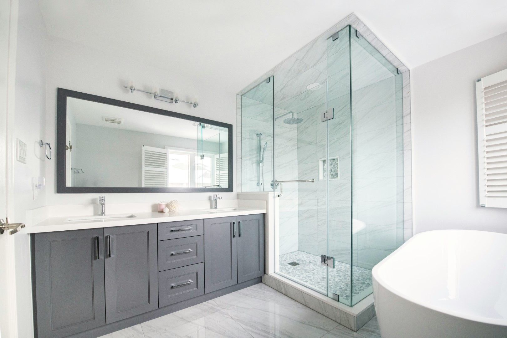 Bathroom with glass shower, gray vanity, freestanding tub, and bright finishes after bathroom remodeling in Avondale, AZ