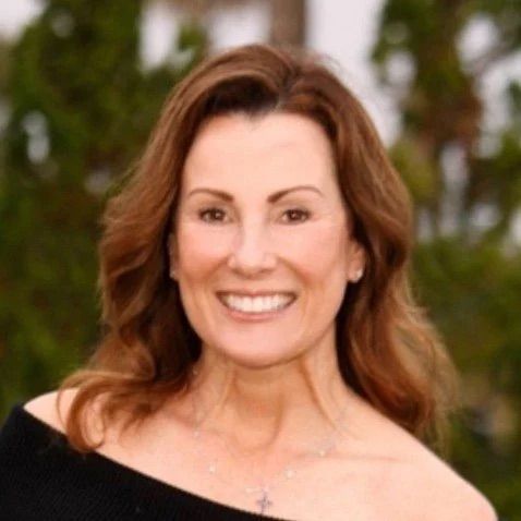 Smiling woman with long brown hair in an off-shoulder black top against a blurred green background