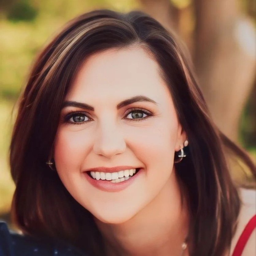 Smiling woman with dark hair outdoors, wearing earrings and a red top.