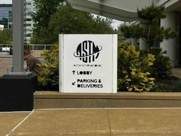 White directory sign with logo and arrows for lobby, parking, and deliveries outside a building