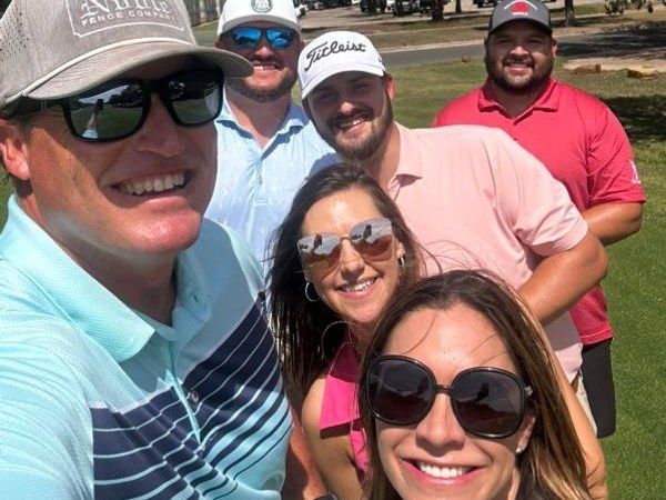 Five smiling friends taking a selfie outdoors, wearing sunglasses and casual golf attire